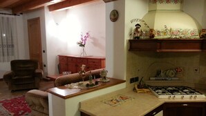 A cozy living room with a fireplace, a dining area with a table, and a kitchen with a stove. - The house in Old Railway 2 (the places of the Great War) (Velo D'astico)
