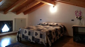A bedroom with a wooden ceiling, a bed with a patterned bedspread, a window with curtains, and a vase with flowers on a nightstand. - The house in Old Railway 2 (the places of the Great War) (Velo D'astico)