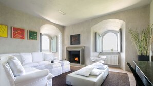 A modern living room with a fireplace, white furniture, and artwork on the walls. - Medioevo&Design, Historical Umbria Tower With Private Pool, gardens, parkings (Todi)