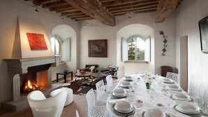 A dining area with a fireplace, white chairs, and a table set for a meal. - Medioevo&Design, Historical Umbria Tower With Private Pool, gardens, parkings (Todi)