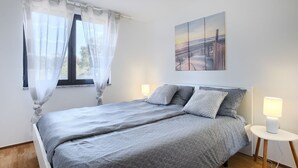 A bedroom with a bed, two bedside tables with lamps, a window with sheer curtains, and a painting on the wall. - Attractive apartment near beach with BBQ (Banjole)