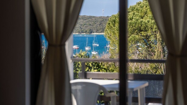 A view from a window with curtains, overlooking a marina with several sailboats and a distant hill with a tower. - Attractive apartment near beach with BBQ (Banjole)