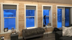 A cozy room with wooden walls, large windows, a telescope, a couch, and a door. - Eagle Lake Fishing - Getaway Cabin (Waldhof)