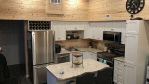 A modern kitchen with wooden walls, stainless steel appliances, a marble countertop, and a clock on the wall. - Eagle Lake Fishing - Getaway Cabin (Waldhof)
