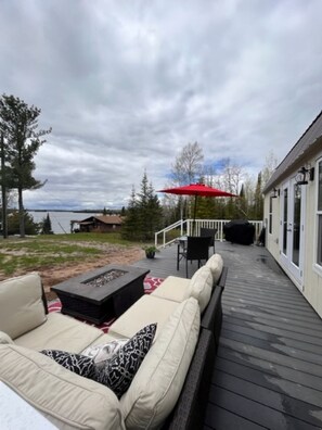 A deck with outdoor furniture, a red umbrella, and a view of a lake. - Eagle Lake Fishing - Getaway Cabin (Waldhof)