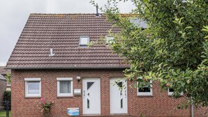 A brick building with two white doors, a small window, and a sign on the ground. - Just let your mind wander: the quiet location of this holiday Doppelha (Carolinensiel)