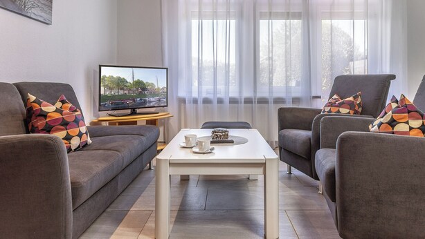 A living room with a sofa, armchairs, a coffee table, a television, and a window with curtains. - Just let your mind wander: the quiet location of this holiday Doppelha (Carolinensiel)
