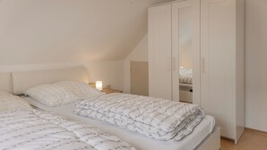 A bedroom with two beds, a wardrobe, and a bedside table with a lamp. - Just let your mind wander: the quiet location of this holiday Doppelha (Carolinensiel)