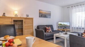 A modern living room with a dining area, a television, and a view of the outdoors. - Just let your mind wander: the quiet location of this holiday Doppelha (Carolinensiel)