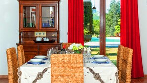 Un coin repas avec des chaises en osier, une table dressée avec des assiettes et des verres, et un buffet en bois doté de portes en verre.