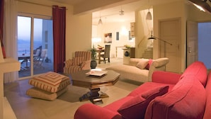Amplia sala de estar con un sofá rojo, un sillón a rayas y una mesa de centro. Se ve un comedor con mesa y sillas al fondo.