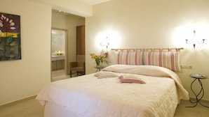 Un dormitorio con una cama grande, una mesita de noche, una silla, una pequeña mesa con un florero y un cuadro en la pared.