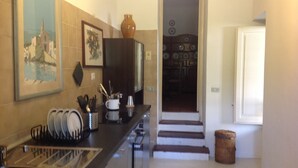 A kitchen with a sink, dish rack, and a cabinet with kitchen utensils. There is a door leading to another room. - Casanatura Capo Mulini, traditional Sicilian rustic surrounded by nature (Acireale CT)