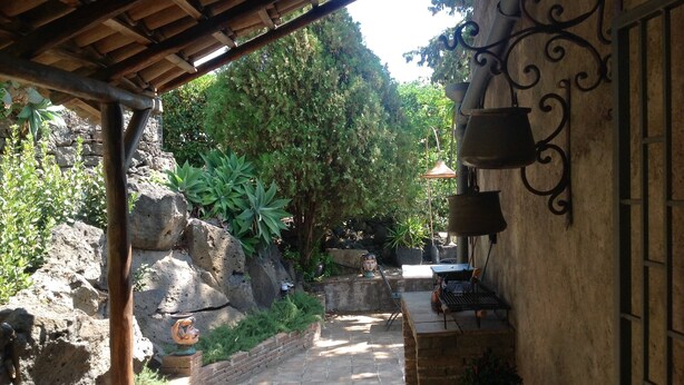 A stone pathway leading to a covered area with a rustic wooden ceiling, surrounded by greenery and rocks. - Casanatura Capo Mulini, traditional Sicilian rustic surrounded by nature (Acireale CT)