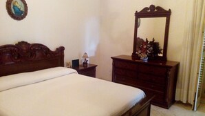 A bedroom with a wooden bed, a dresser, a mirror, and a small table with a lamp.