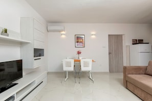 A modern living room with a flat-screen TV, white furniture, a dining area with two chairs, a table, and a beige sofa. - Apartment with large pool, WiFi in the resort of Pula (Pula)