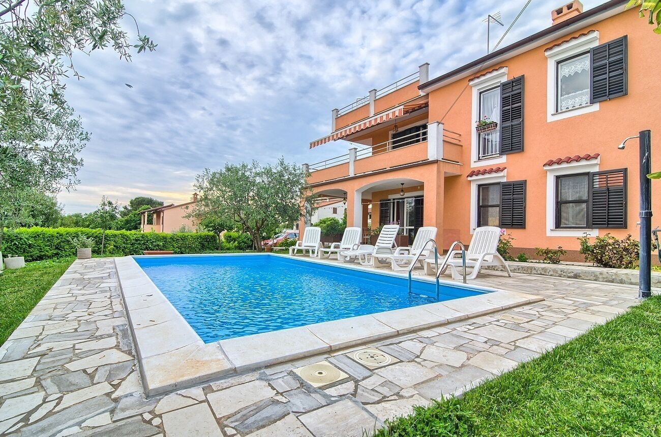 A two-story house with a swimming pool, stone pathway, and outdoor seating area.