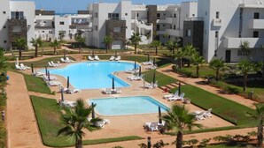 A resort with a central swimming pool surrounded by sun loungers and palm trees. - Beautiful apartment in La Perla 2 4332 (Saidia)
