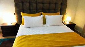 Un lit avec une tête de lit capitonnée, deux oreillers blancs et un plaid jaune.