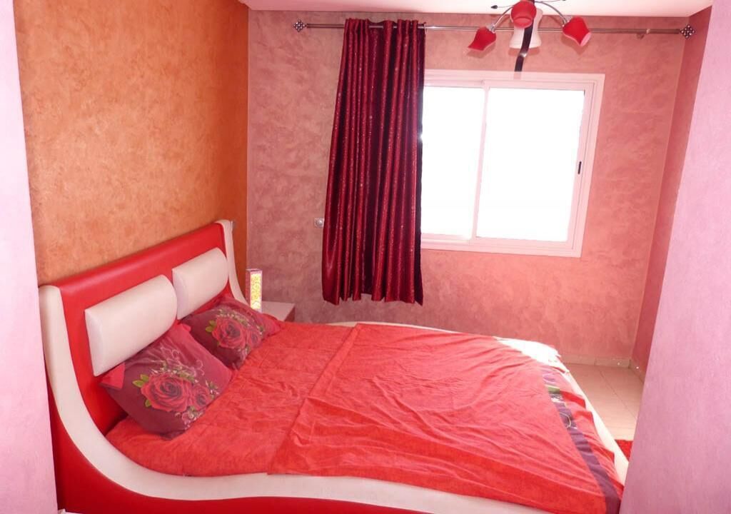 Una camera da letto con un letto, una finestra con tende e un comodino con una lampada.