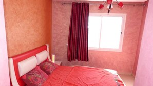 Une chambre à coucher avec un lit, une fenêtre avec des rideaux et une table de chevet avec une lampe.