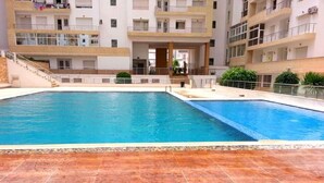 Une piscine dotée d’une plage carrelée, entourée d’un immeuble résidentiel à plusieurs étages avec des balcons.