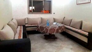 A living room with a sofa set, a coffee table, and a window with blinds. - Nice apartment in Réidence Attadamon 4470 (Agadir)