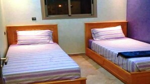 Two single beds with wooden headboards and striped bedding in a room with a window and a purple wall. - Nice apartment in Réidence Attadamon 4470 (Agadir)