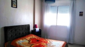 Une chambre à coucher avec un lit, une table de chevet, une lampe et une fenêtre avec des rideaux.