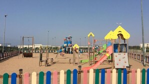 Een strand speeltuin met diverse speeltoestellen, zoals glijbanen en schommels, omgeven door een houten hek.