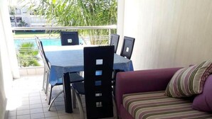 Een kamer met een eettafel en stoelen, een paarse bank en uitzicht op een zwembad.
