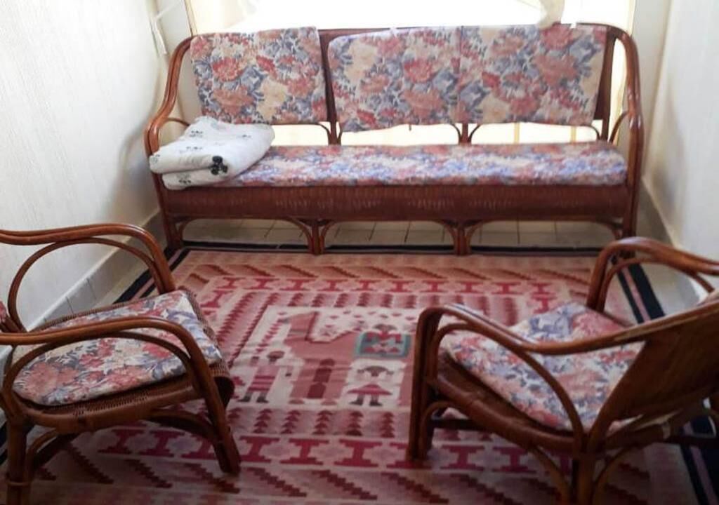 A room with a sofa and two chairs, a patterned rug, and a window with curtains.