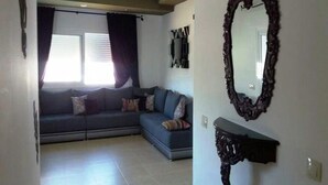 Una sala de estar con un sofá de color oscuro, un espejo grande y una estantería de pared.