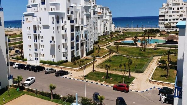 Un hotel moderno con varios pisos, un estacionamiento y una piscina con vistas al mar.
