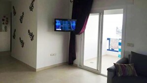 Una sala de estar con un televisor de pantalla plana montado en la pared, un puerta corrediza de vidrio y un sofá de color oscuro.