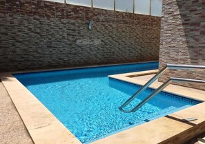 A swimming pool with a stone wall backdrop and a metal ladder.