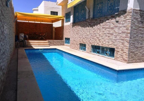 A swimming pool with a yellow canopy, stone walls, and blue decorative elements.