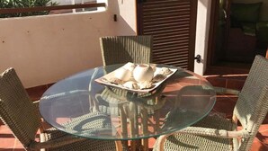 Ein Tisch mit Glasplatte und Korbstühle auf einem Balkon.