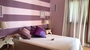 Ein Schlafzimmer mit einem Bett, einem Nachttisch, einer Lampe und einem Fenster mit Vorhängen.
