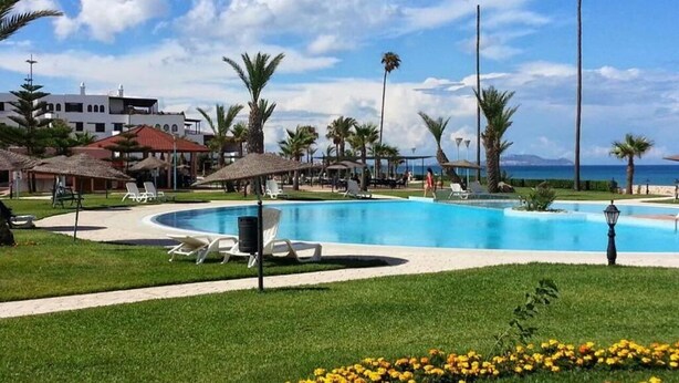 Ein Poolbereich mit Liegestühlen, Palmen und freiem Blick auf das Meer.