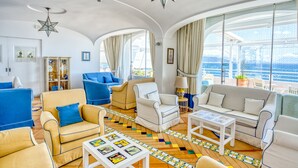 A spacious living room with a large window, a star-shaped light fixture, and a colorful floor design. - Hotel Cetus (Cetara)