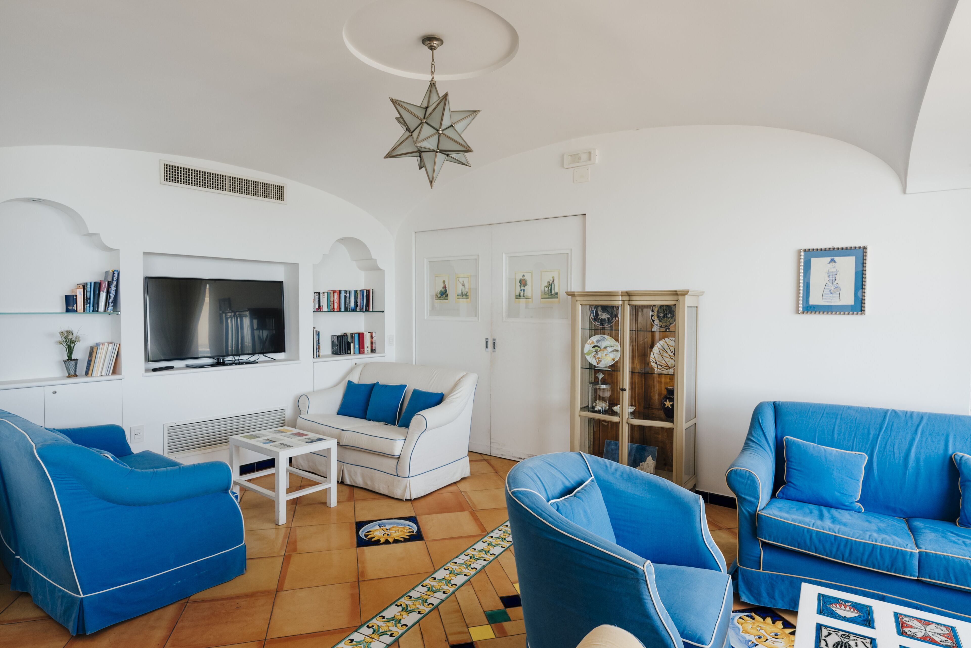 Un soggiorno con un divano bianco, poltrone blu, un tavolino da caffè, una TV e una stella decorativa appesa al soffitto.