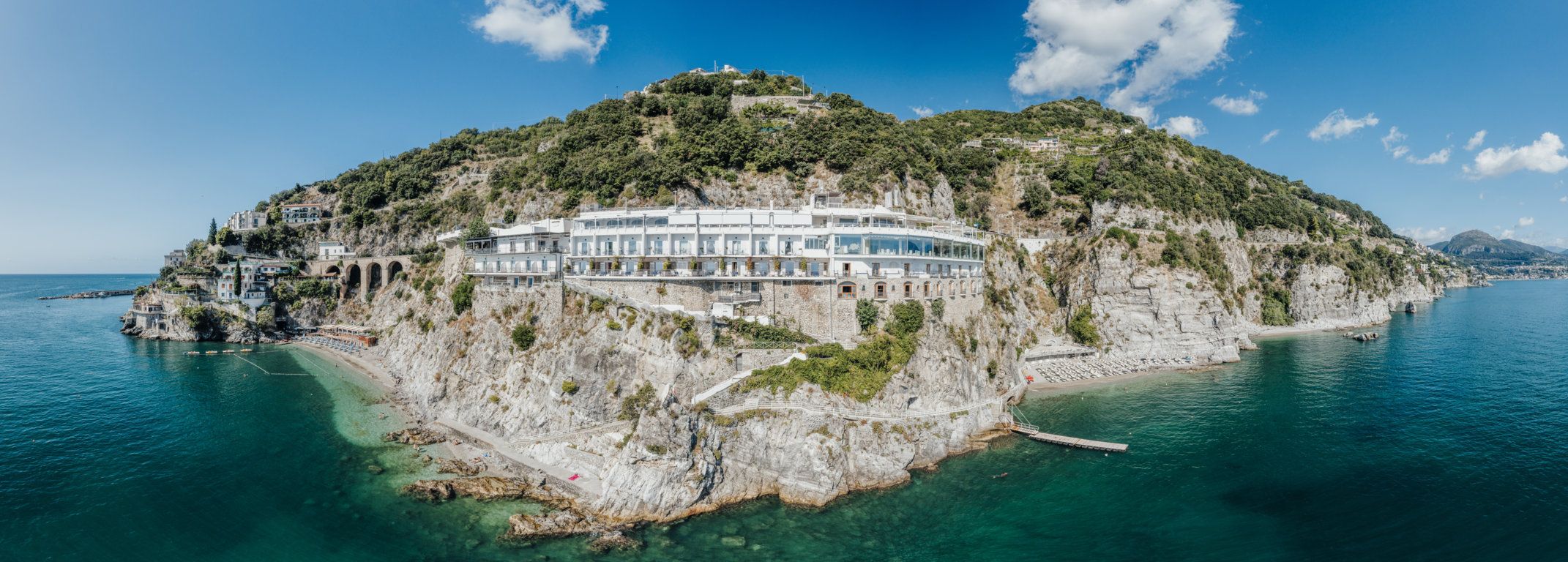 Una proprietà costiera con un edificio grande, un litorale roccioso e acque blu cristalline.