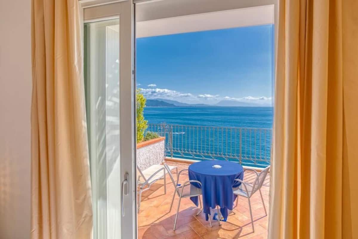 A balcony with a table and chairs, overlooking a sea view.