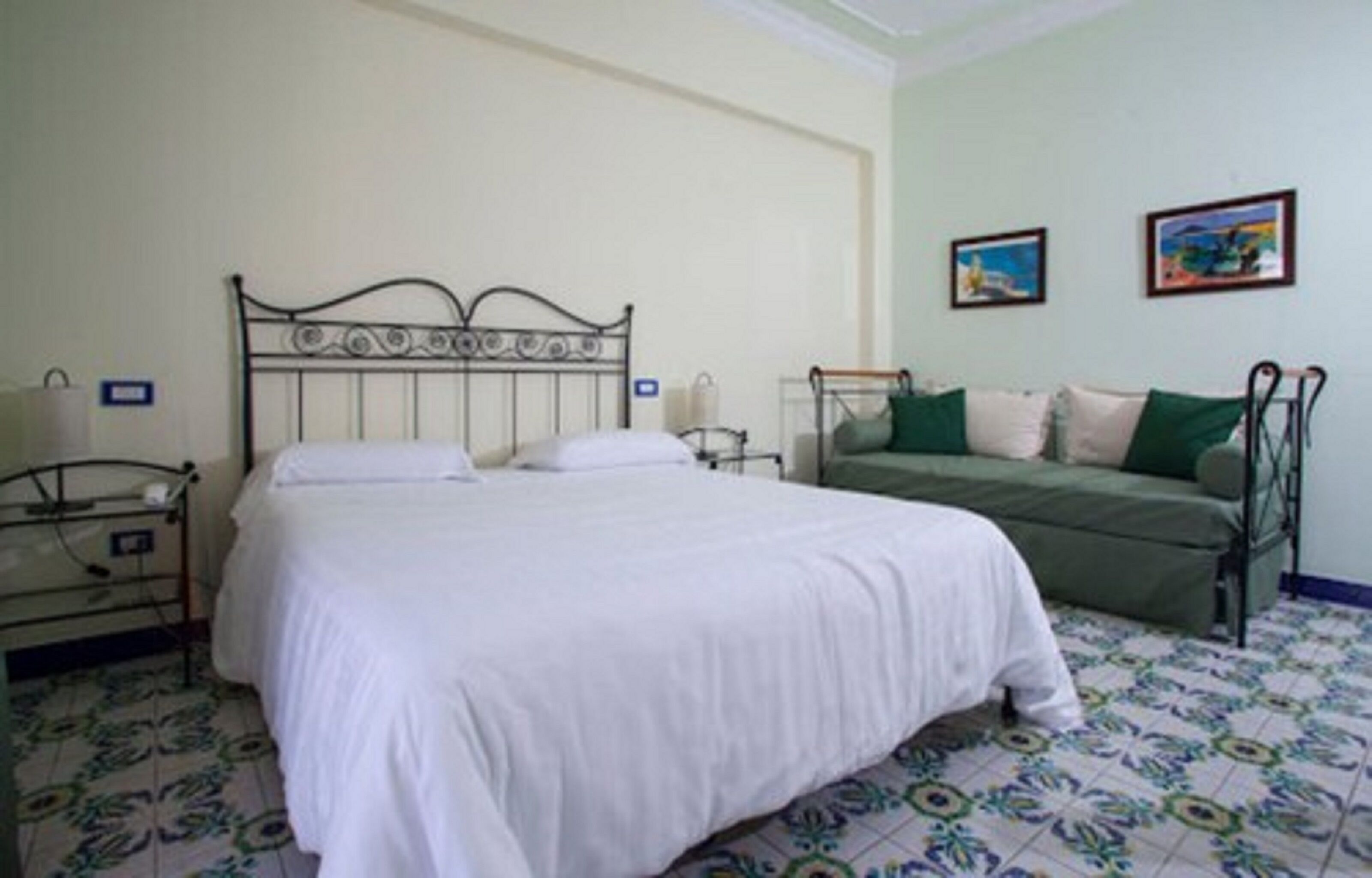 A bedroom with a bed, a green sofa, and two framed pictures on the wall.