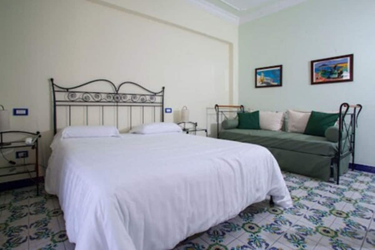 A bedroom with a metal bed frame, a green sofa, and a patterned floor.