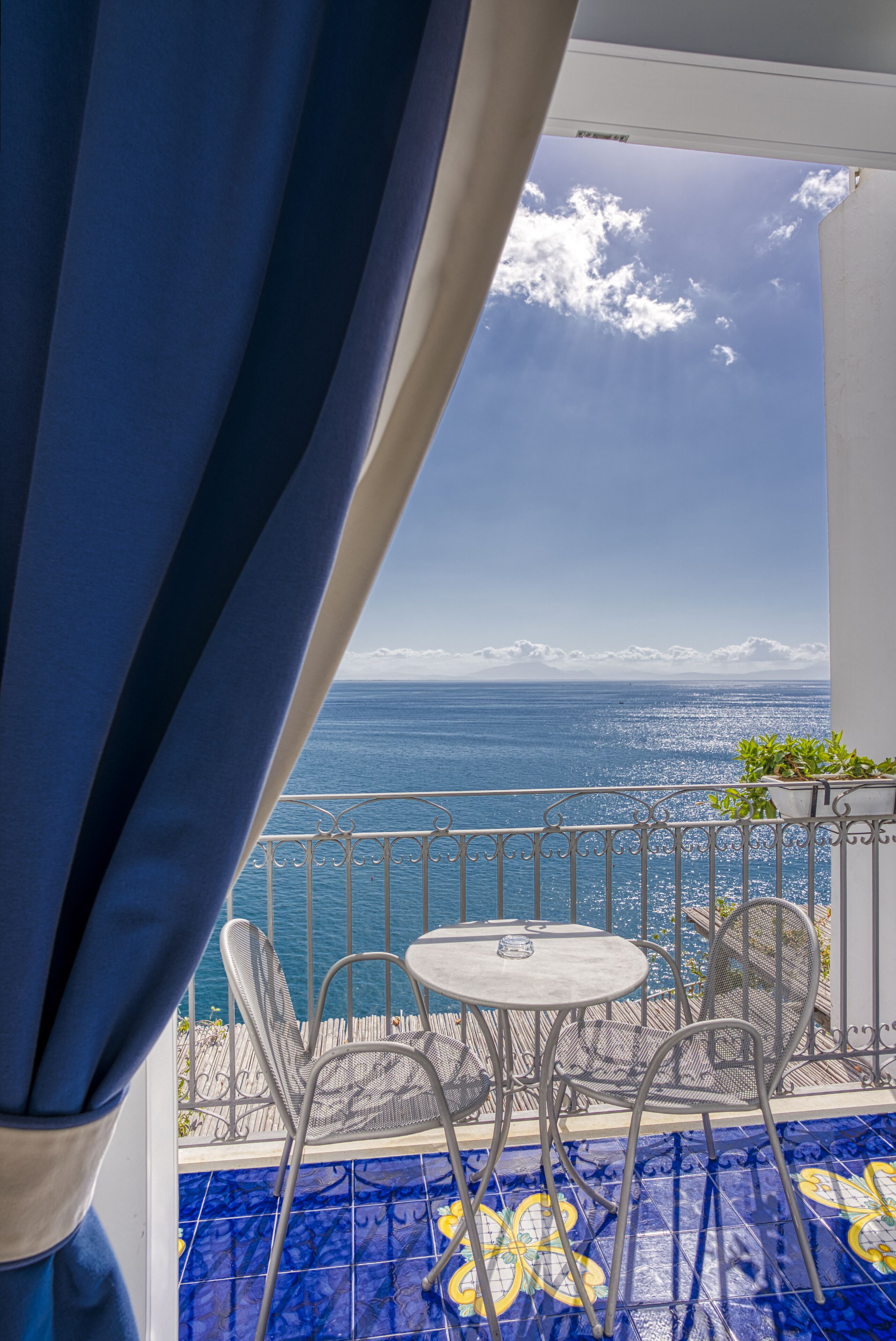 A balcony with a view of the sea, a small table, and chairs.