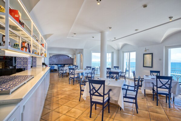 Un restaurante con terraza, mesas y sillas blancas, y piso de baldosas.