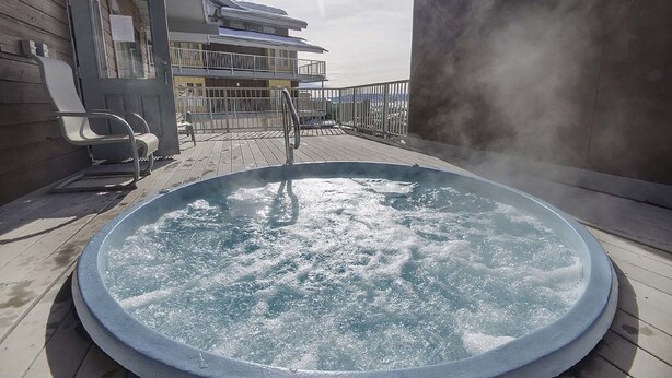 Un jacuzzi en una terraza de madera con vistas a un edificio al fondo.