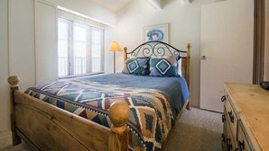 Un dormitorio con una cama de madera, un edredón estampado, una lámpara y un aparador.